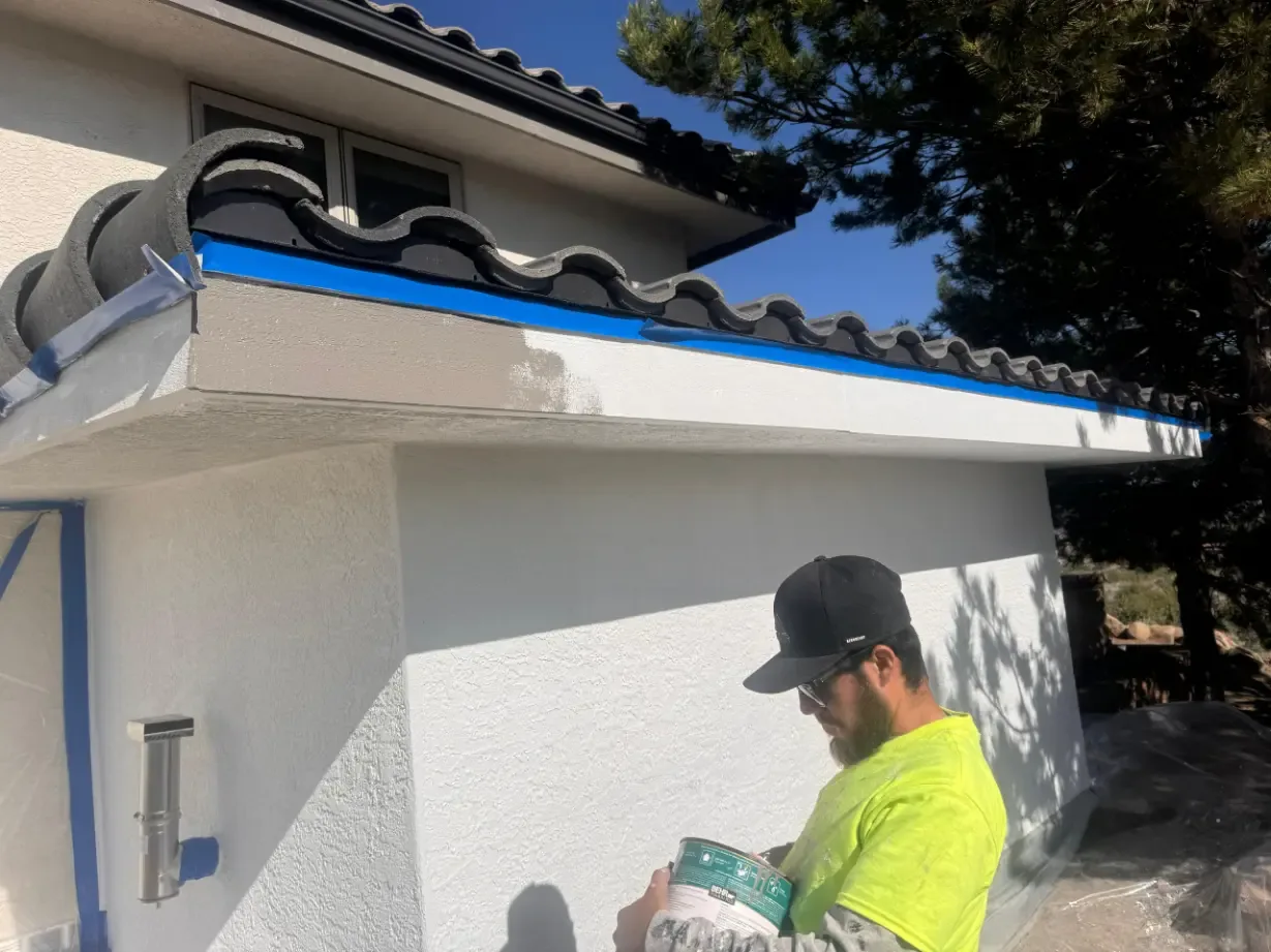 Painter coating white stucco eave with blue tape on roof tiles in Reno, NV