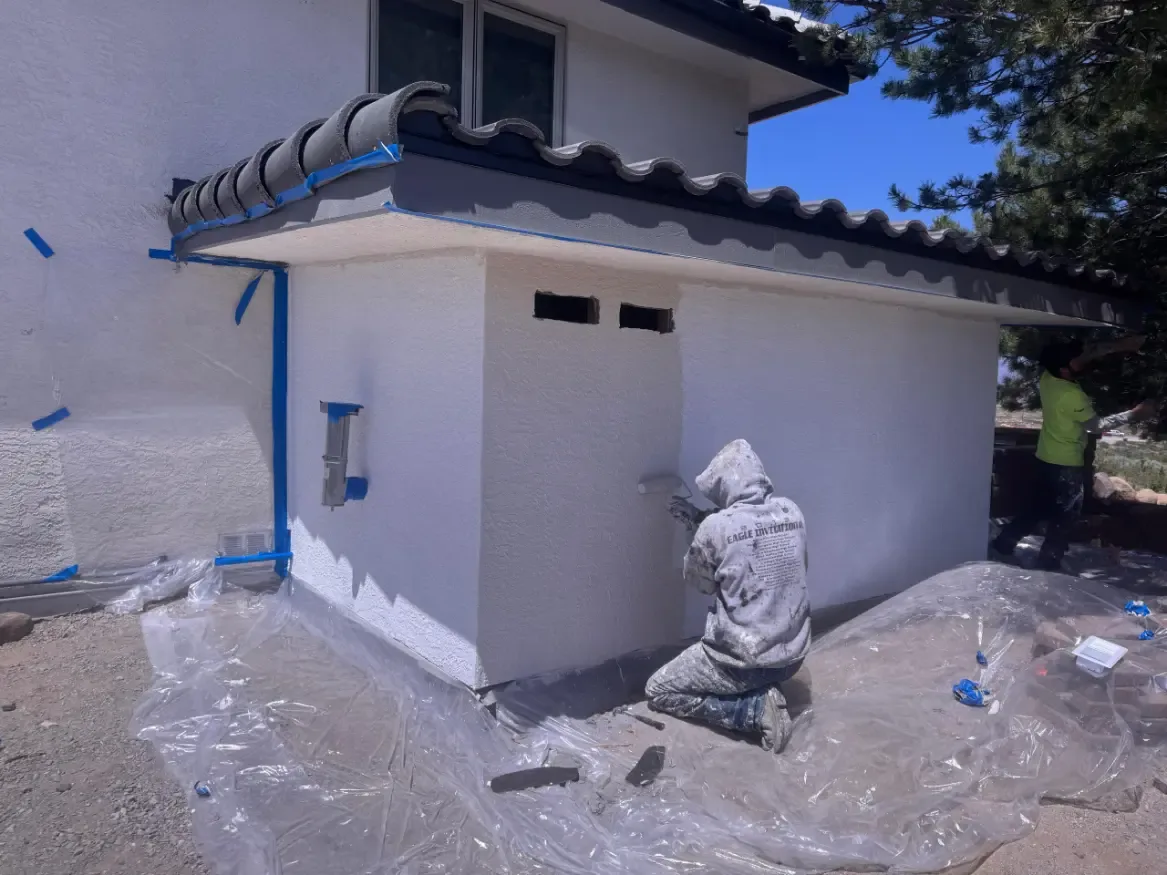 Crew painting white stucco exterior with taped-off roof tiles in Reno, NV