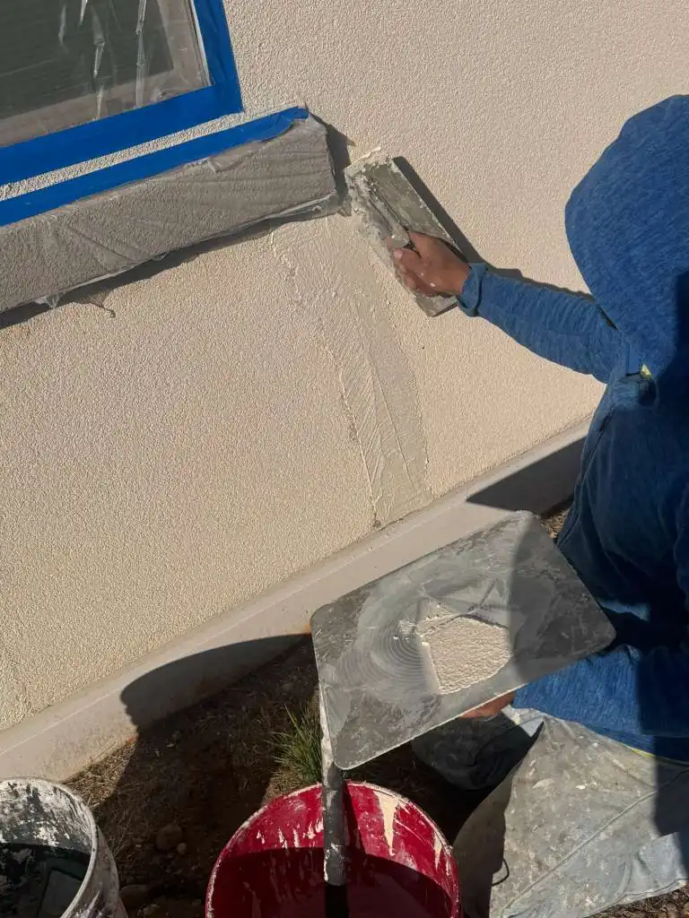 Worker hand-troweling stucco around a taped window during exterior repair in Reno, NV
