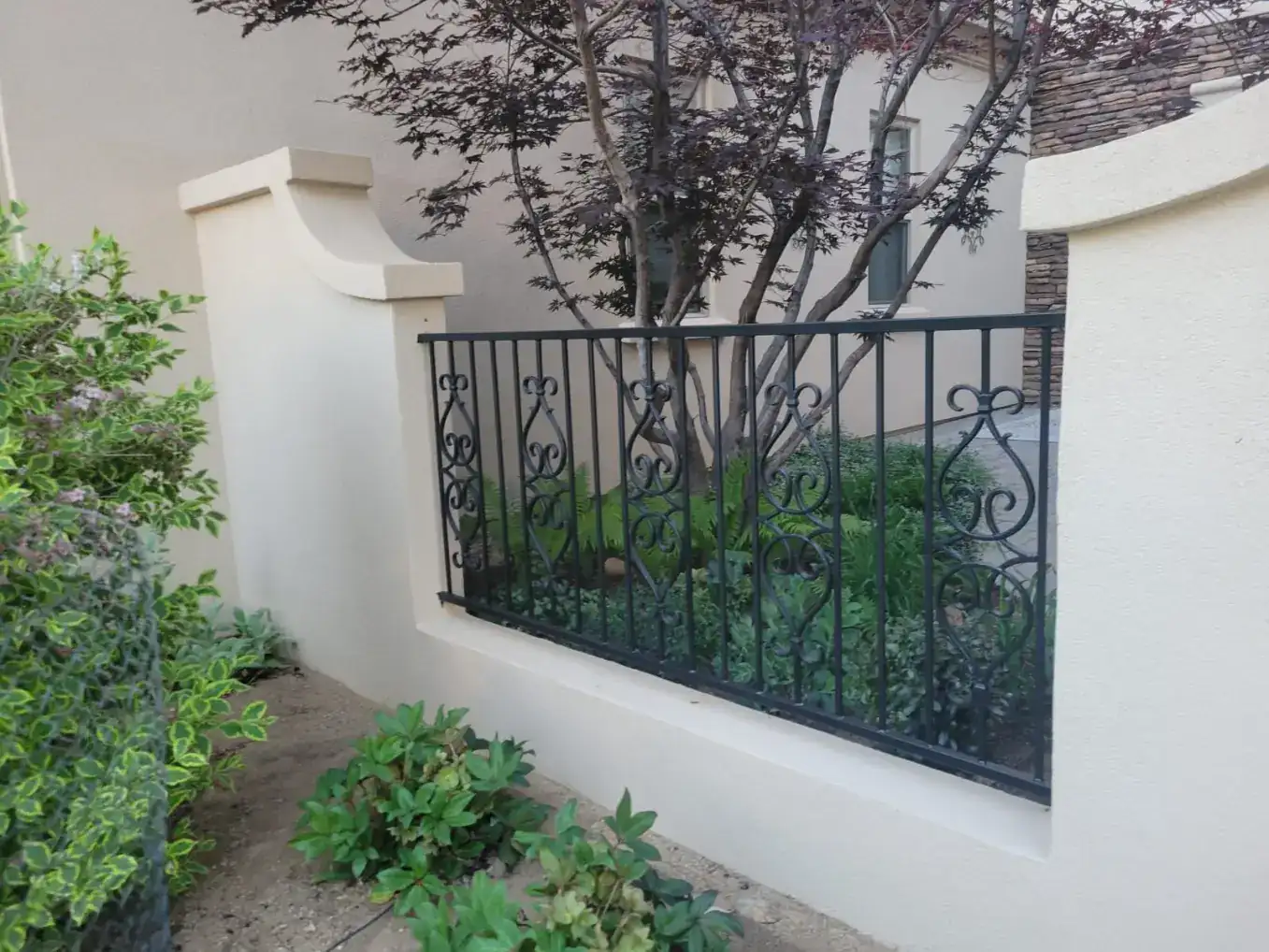 Smooth finished cream stucco garden wall with decorative black iron railing in Reno, NV